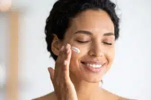 Femme souriante appliquant une crème hydratante sur la joue