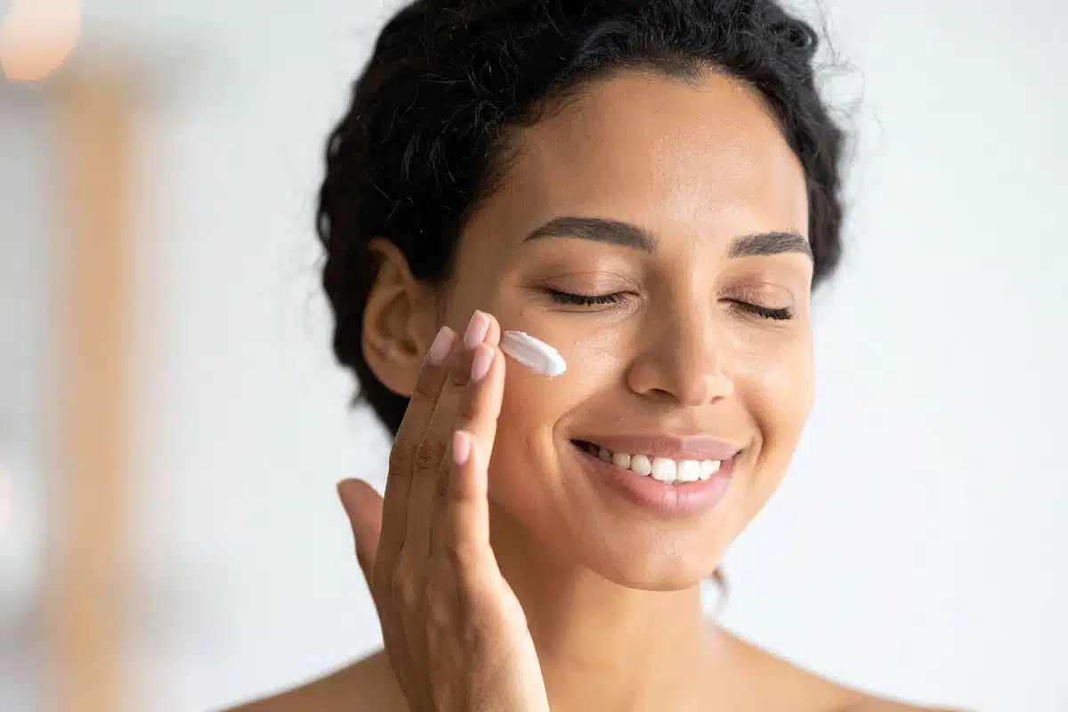 Femme souriante appliquant une crème hydratante sur la joue Femme souriante appliquant une crème hydratante sur la joue