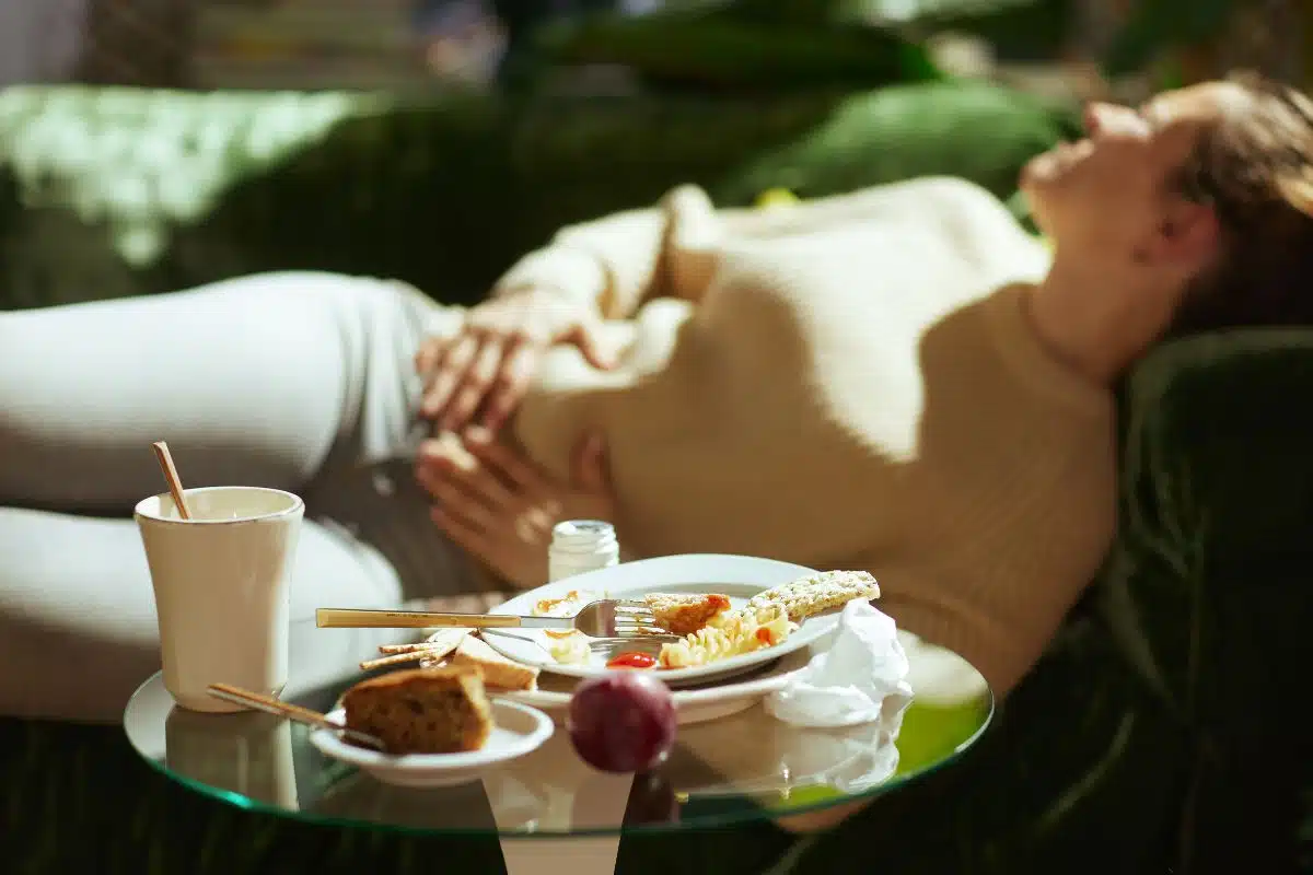Femme allongée sur un canapé avec les mains sur le ventre gonflé après un repas riche en FODMAP