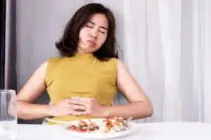 Jeune femme assise à table avec une main sur le ventre, ressentant des ballonnements après le repas