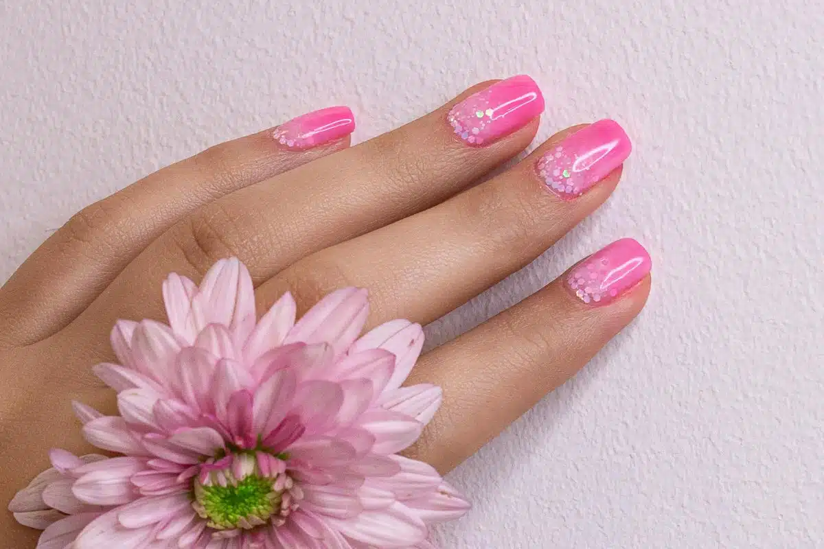 Manucure rose dégradée à finition glitter, gros plan sur des ongles courts