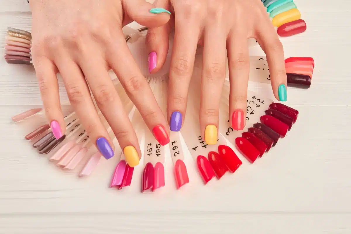 Mains aux ongles colorés posées sur un nuancier de vernis en éventail