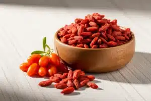 Baies de goji séchées dans un bol en bois avec quelques fruits frais, illustrant ce fruit traditionnel de la médecine chinoise