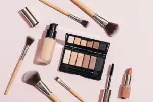 Maquillage du quotidien, produits et pinceaux disposés à plat sur fond rose poudré