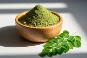 Poudre de moringa dans un bol en bois avec des feuilles de moringa fraîches, illustrant ce super-aliment africain