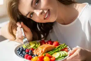 Alimentation anti-rides : femme à la peau lumineuse avec une assiette colorée de saumon, baies et avocat