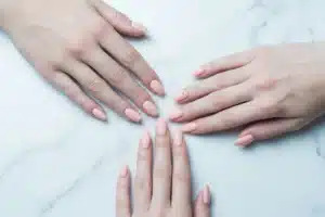 Quatre mains montrant les formes d'ongles ronde, carrée, amande et coffin sur fond marbre blanc