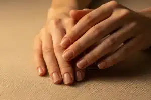 Deux mains aux ongles naturels brillants posés sur un tissu de lin écru, résultat d'une manucure japonaise