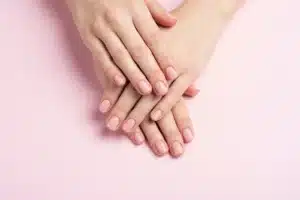 Mains féminines aux ongles courts et soignés après une manucure russe, vue de dessus sur fond rose poudré