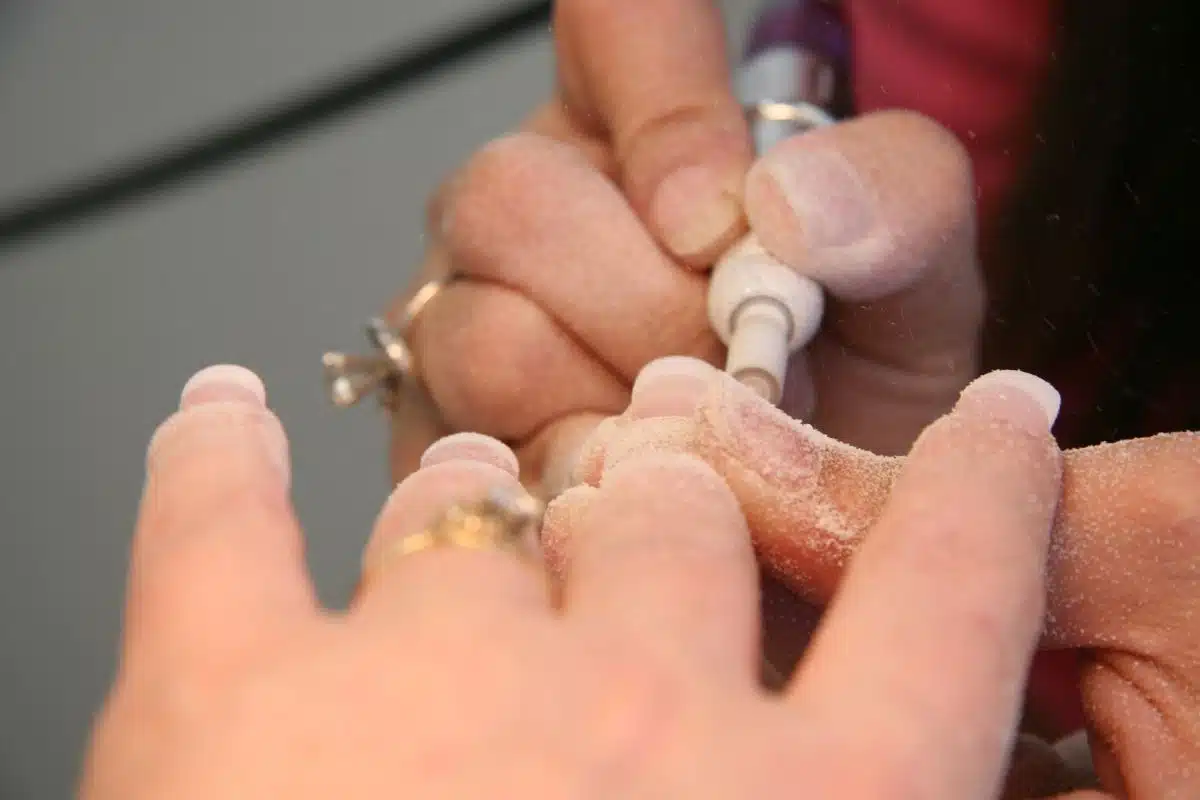Utilisation d'une ponceuse à ongles en gros plan Gros plan de mains en train de poncer un ongle avec une ponceuse électrique, poussière de ponçage visible