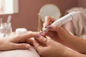 Main utilisant une ponceuse électrique sur un ongle à 45 degrés, technique correcte de manucure