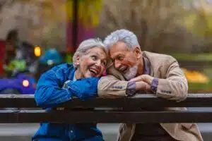 Couple de seniors complices et souriants sur un banc en extérieur, symbole d'une retraite sereine