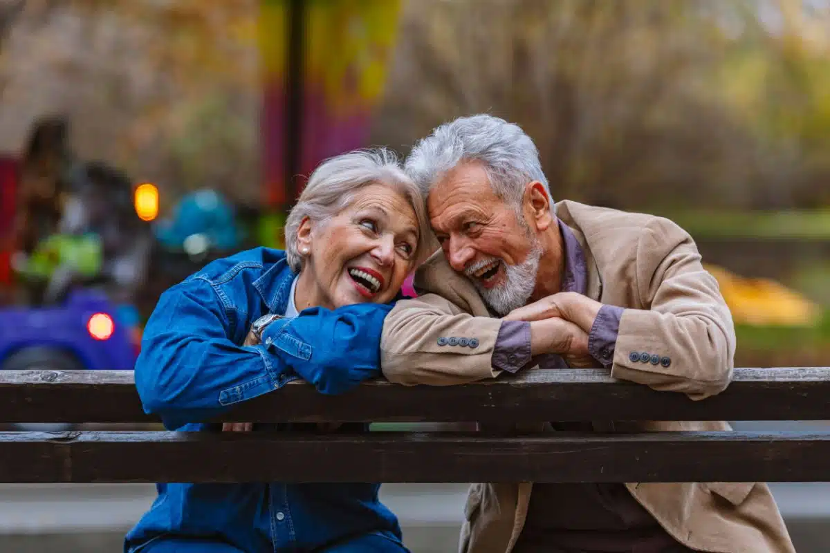Couple de seniors souriants profitant de leur retraite Couple de seniors complices et souriants sur un banc en extérieur, symbole d'une retraite sereine