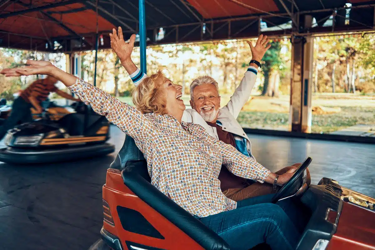 Couple de seniors riant, bras levés, sur une auto tamponneuse