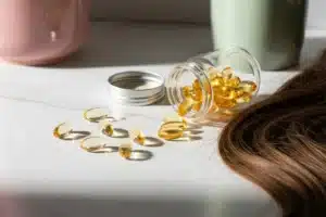 Compléments alimentaires pour cheveux : gélules dorées sortant d'un flacon près d'une mèche de cheveux brillants