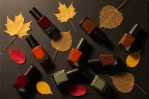 Flacons de vernis à ongles bordeaux, terracotta et marron sur ardoise avec feuilles séchées, palette automnale