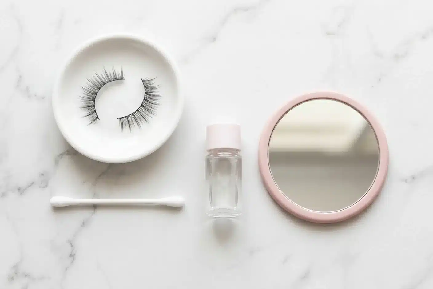 Accessoires d'entretien et nettoyage des faux cils Accessoires d'entretien des faux cils posés sur marbre blanc : paire de cils, coton-tige, démaquillant et miroir