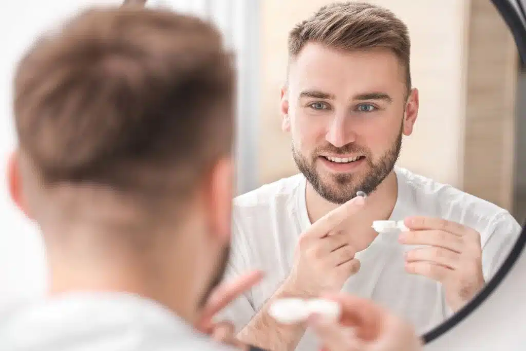 Homme posant une lentille de contact devant le miroir de sa salle de bains