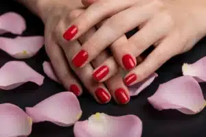 Mains avec vernis rouge cerise pour la Saint-Valentin, pétales de rose