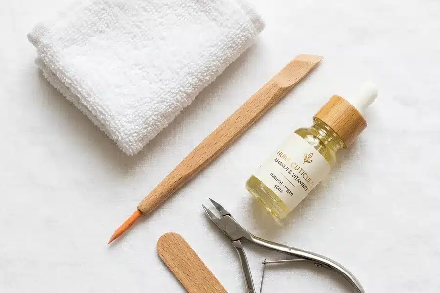 Flat lay d'outils pour soin des cuticules : repousse-cuticules en bois, huile pour ongles, serviette blanche