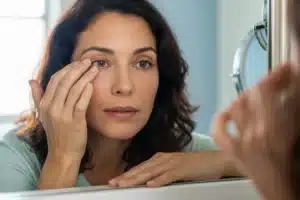 Femme touchant sa paupière gonflée devant un miroir de salle de bain