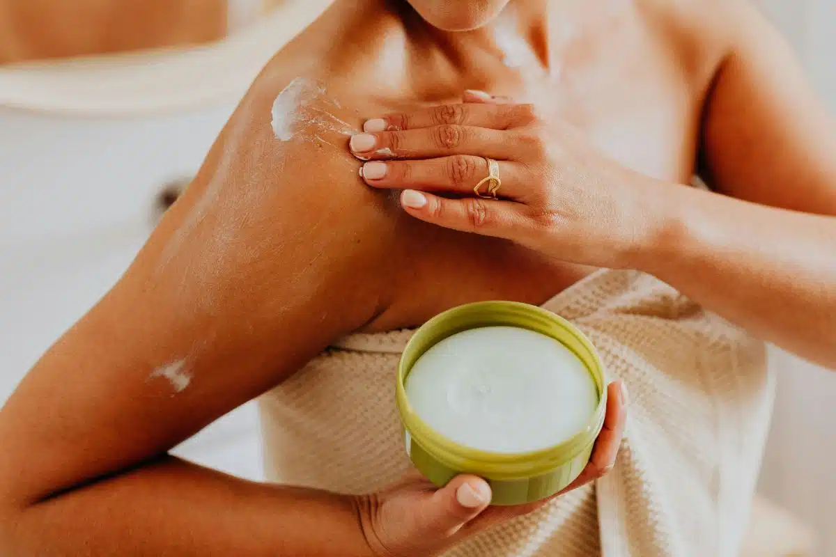 Application d'une crème hydratante sur l'épaule Femme appliquant une crème émolliente sur son épaule après la douche