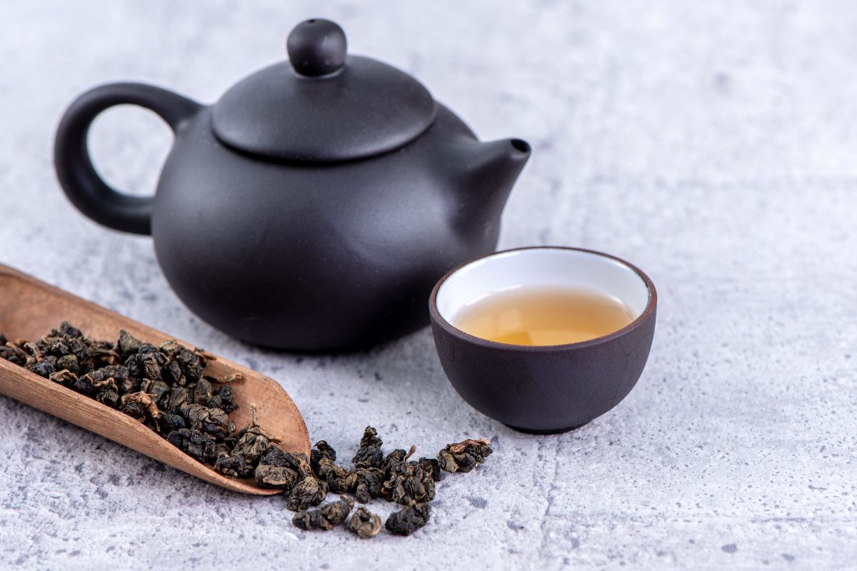 Théière noire en céramique, bol de thé et feuilles de thé oolong roulées sur une cuillère en bois