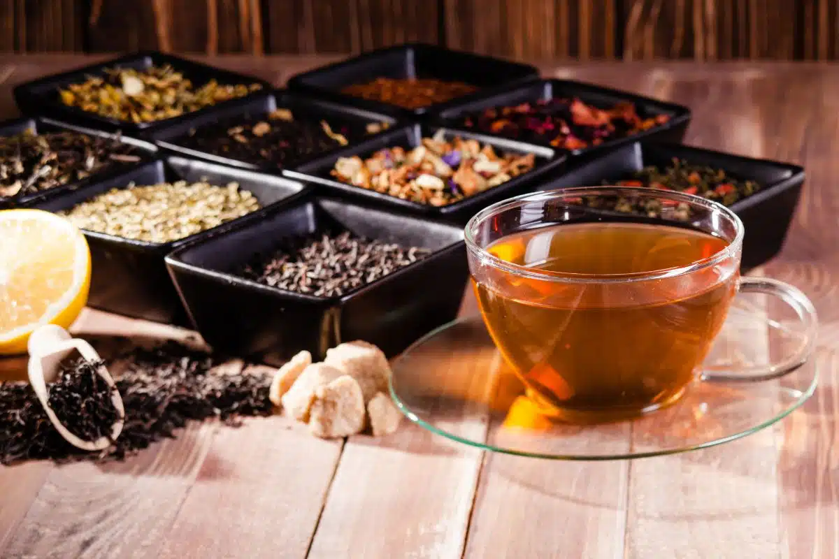 Assortiment de thés en vrac dans des coupelles (thé vert, thé noir, rooibos, fleurs) et tasse de thé