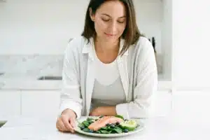 Femme regardant son assiette anti-acné avec saumon, myrtilles, épinards et avocat dans une cuisine lumineuse