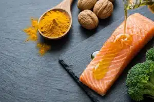 Flat-lay de curcuma, saumon, noix et brocoli sur fond ardoise, alimentation anti-inflammatoire pour l'arthrose