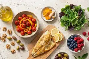 Table garnie d'aliments anti-inflammatoires : huile d'olive, légumes colorés, poisson, curcuma et fruits rouges