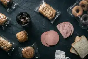 Aliments ultra-transformés sur une surface sombre : viennoiseries, soda, charcuterie et pain de mie