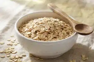 Bol de flocons d'avoine crus avec cuillère en bois, fond lin pâle