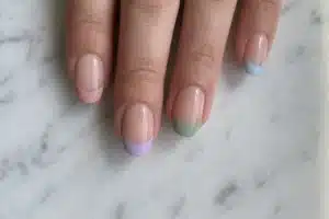 Vue de dessus d'ongles avec french manucure couleur en rose, lilas et vert sauge sur marbre blanc