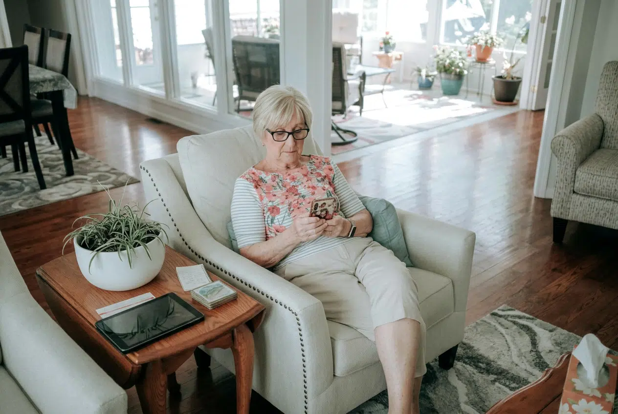 Femme âgée installée dans un fauteuil de son salon, consultant son smartphone à domicile