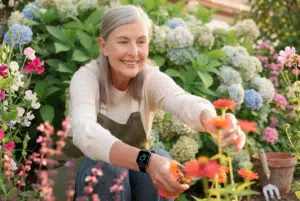 Femme senior souriante jardinant en extérieur, une montre connectée au poignet
