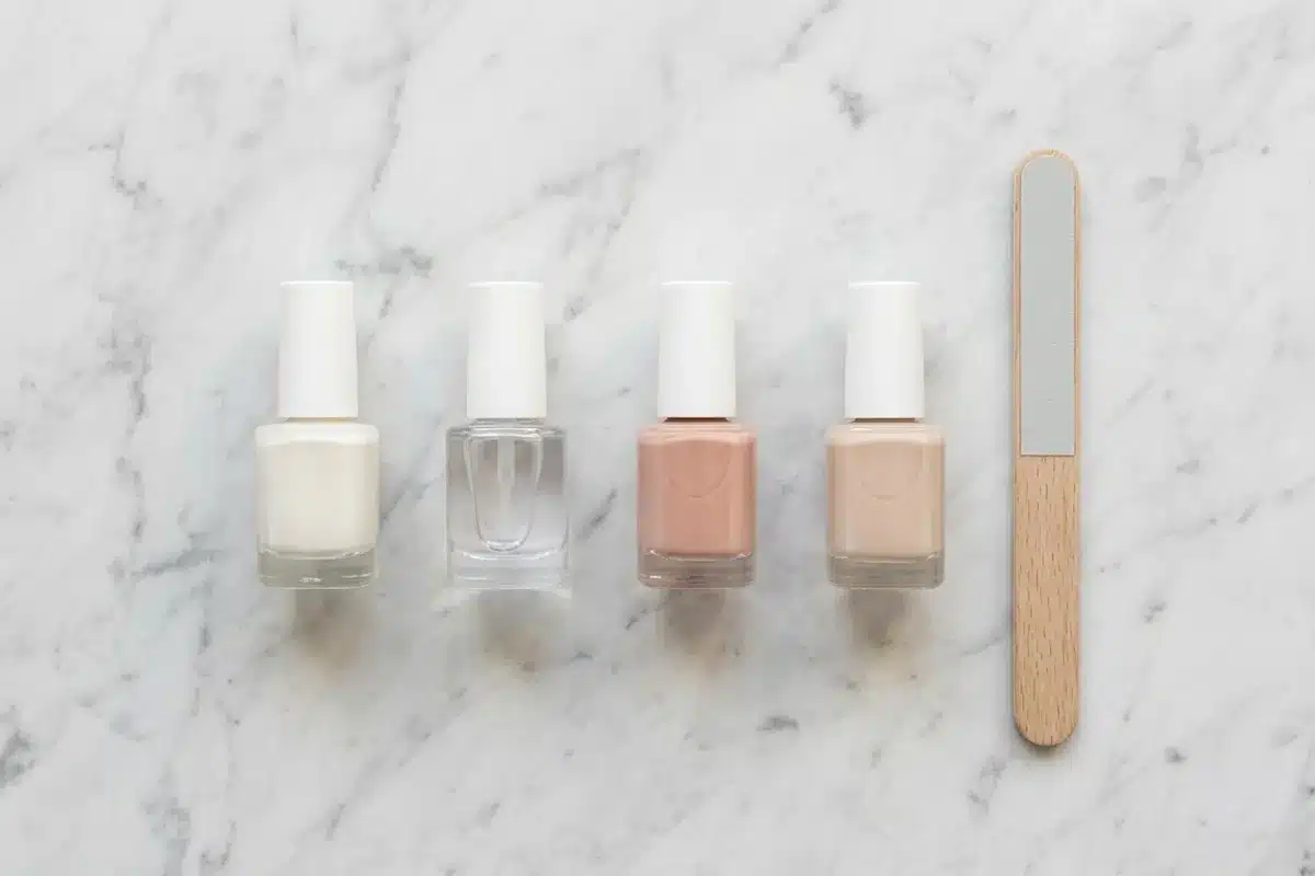 Produits pour french manucure fine Vue de dessus de vernis nude, blanc et top coat posés sur du marbre blanc pour réaliser une french manucure fine