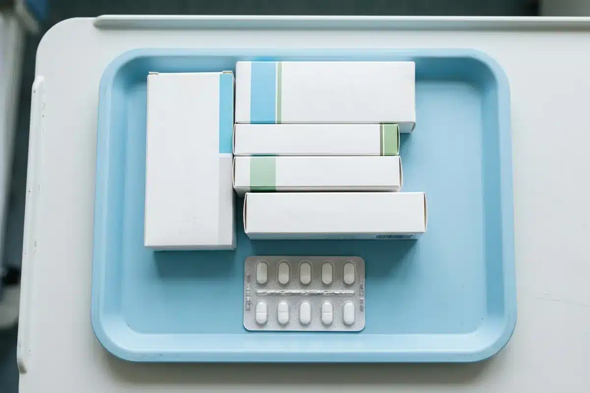 Boîtes de médicaments blanches et blister de comprimés sur plateau médical bleu, illustrant l'impact des traitements sur la coloration dentaire