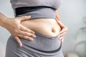 Femme tenant la peau de son ventre, illustrant la prise de poids abdominale à la ménopause