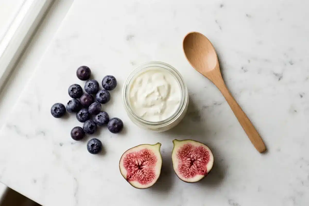 Probiotiques et alimentation pour une flore vaginale équilibrée Yaourt nature, myrtilles et figues coupées sur marbre blanc pour illustrer les probiotiques qui rééquilibrent la flore vaginale